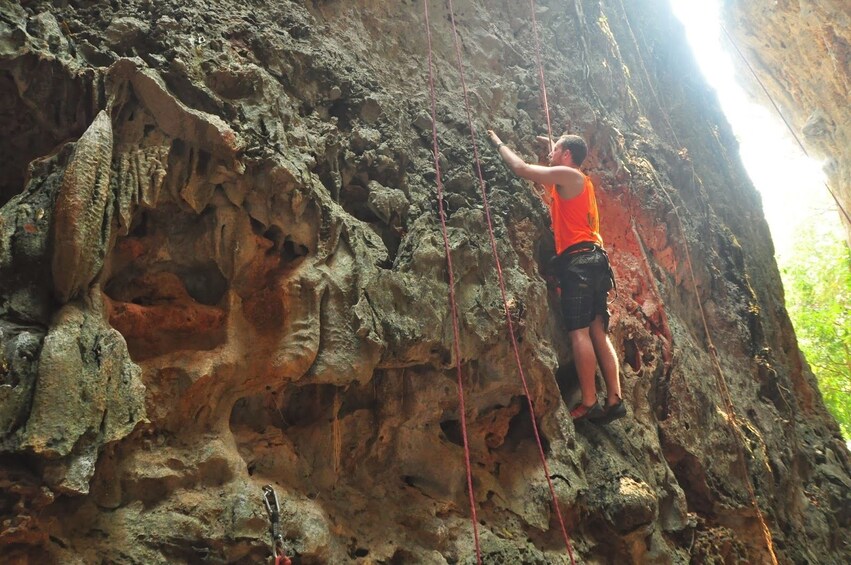 Man in orange shirt rock climbs in Vang Vieng, Laos