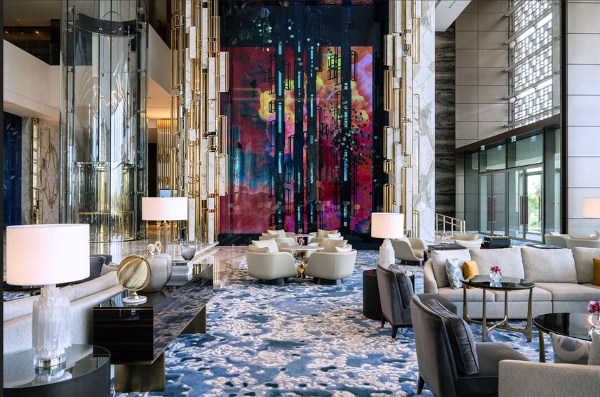 Un lobby lujoso con un cuadro abstracto de gran tamaño, asientos mullidos y una alfombra estampada. 3