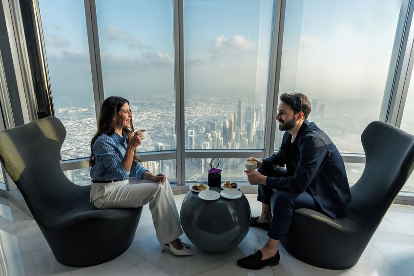 Dos personas sentadas en sillas modernas dentro de un edificio de gran altura, con vista a un paisaje urbano. 5