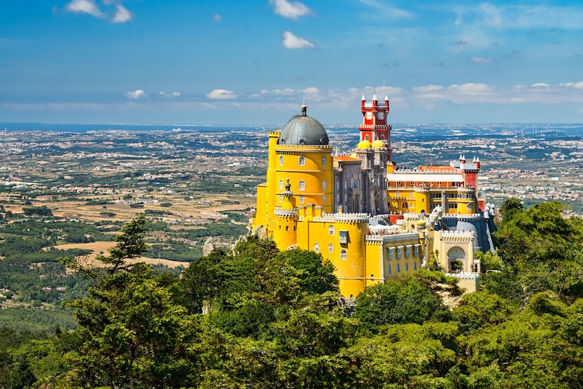 A yellow castle with a red tower and a dome, surrounded by greenery and overlooking a city. 3