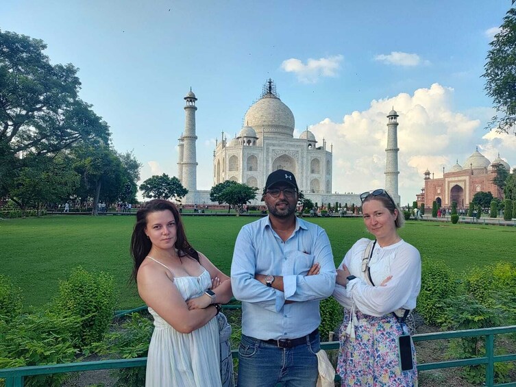 Drei Personen stehen vor dem Taj Mahal, mit Kuppeln und Minaretten im Hintergrund. 1