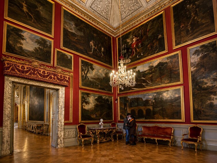 Une pièce somptueuse aux murs rouges, ornée de tableaux encadrés d’or et de meubles richement décorés. 5