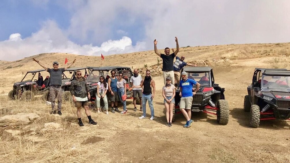 A group of people standing on a dirt road with off-road vehicles parked nearby. 5
