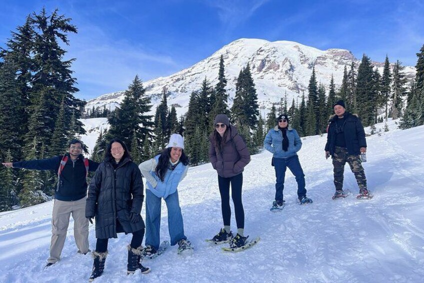 A group of people standing on a snowy mountain with trees and a mountain in the background. 3