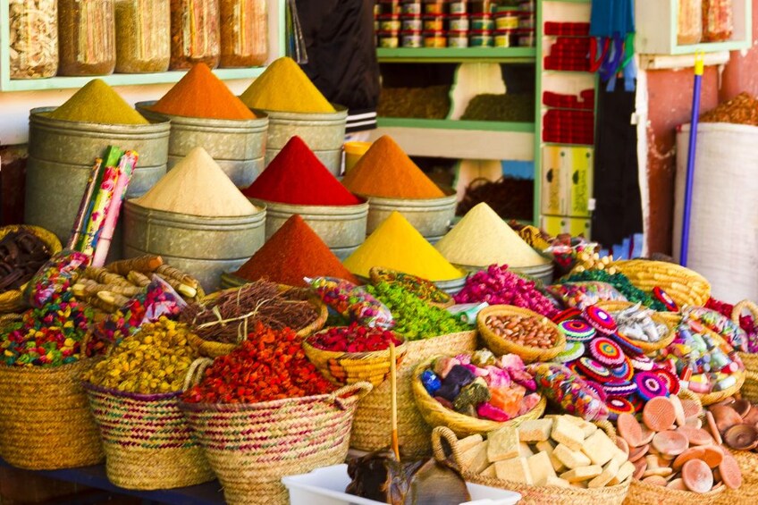 A market stall with colorful spices and dried goods displayed in woven baskets and metal cones. 1