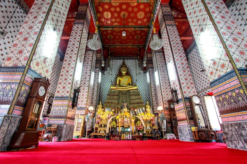 A richly decorated temple interior with a large golden statue, intricate wall patterns, and a red carpet. 4