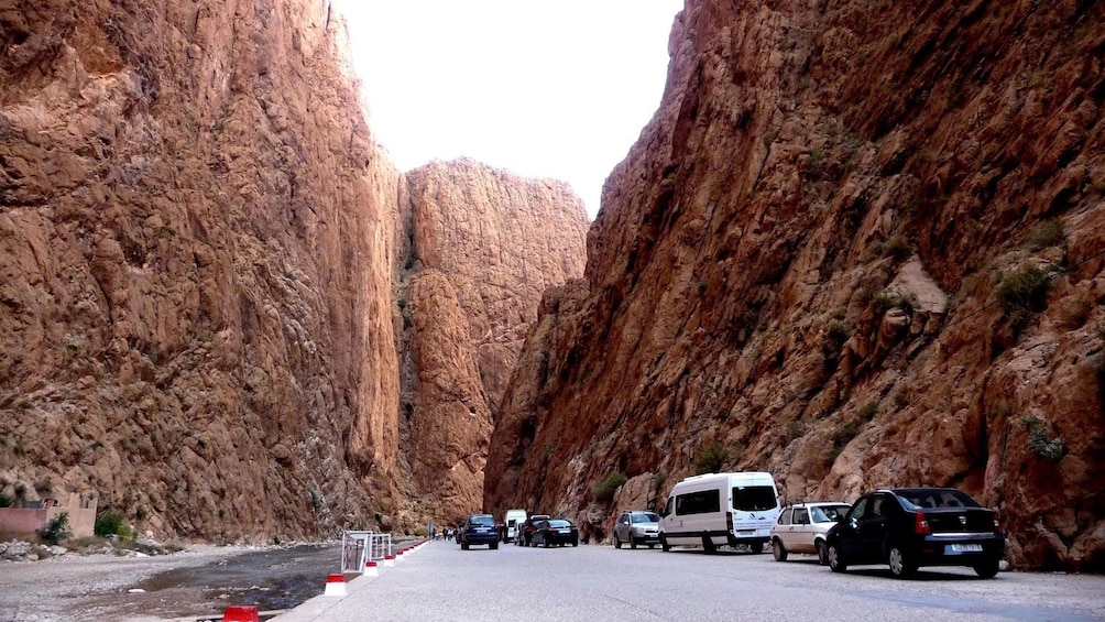 Una strada costeggiata da ripidi dirupi rocciosi, con veicoli parcheggiati lungo il lato della strada. 3