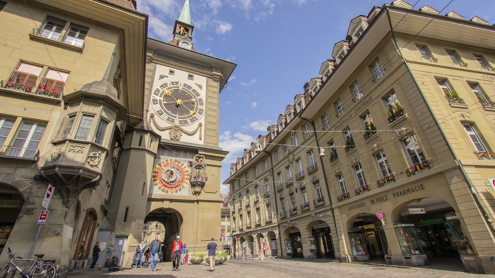 A historic building with a large clock tower, ornate decorations, and a street with pedestrians and shops. 2