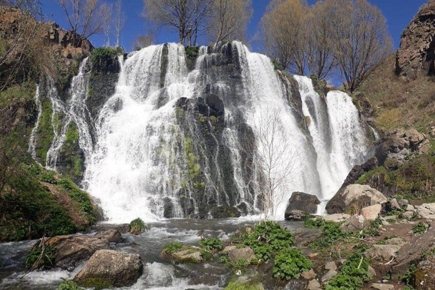 A multi-tiered waterfall surrounded by rocky terrain and sparse vegetation. 2