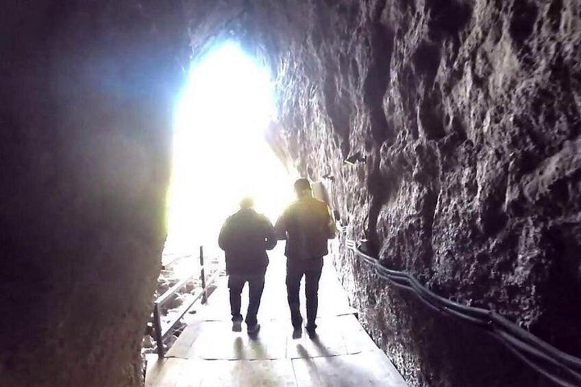 Two people walking through a cave passage with a bright light at the end. 5