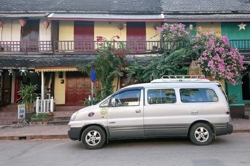 En beige minivan parkeret foran en farverig bygning med en balkon. 1