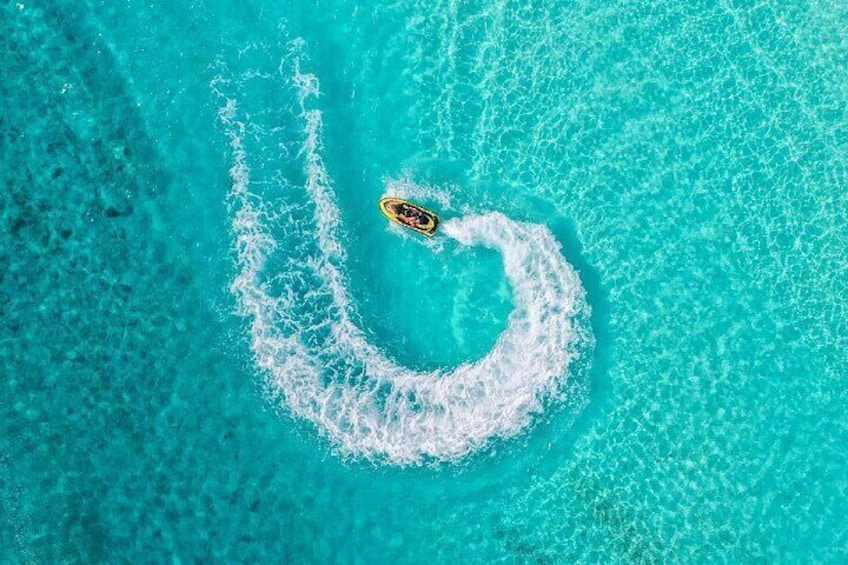 A small boat creating a circular wake in turquoise water. 3