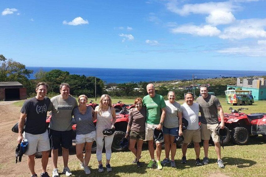 A group of people standing on a grassy field with a view of the ocean and a red vehicle in the background. 5