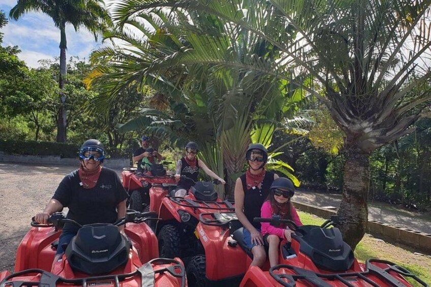 Four people on red ATVs in a tropical setting with palm trees. 2