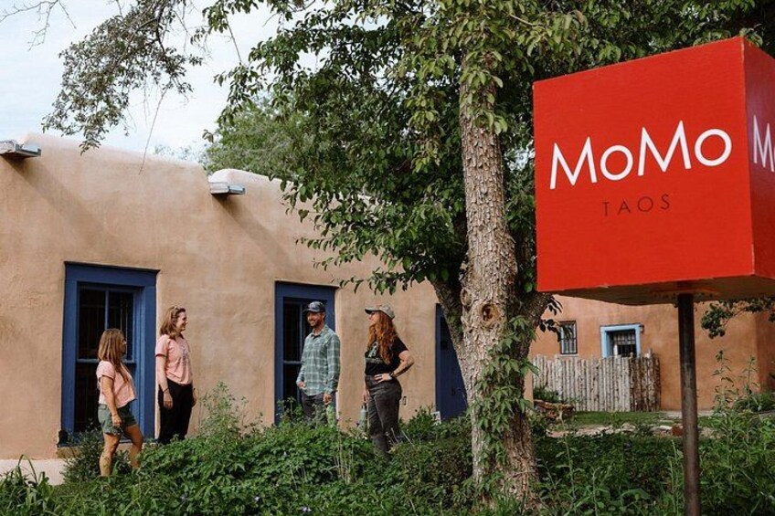 A building with a red sign reading 'MoMo Taos' and a group of people standing in front of it. 4