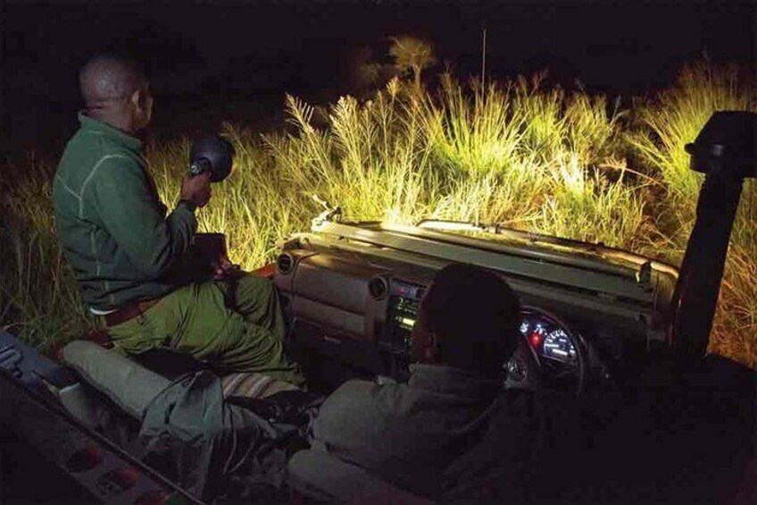 Zwei Personen sitzen in der Nacht neben einem Fahrzeug, eine Person hält eine Taschenlampe. 5