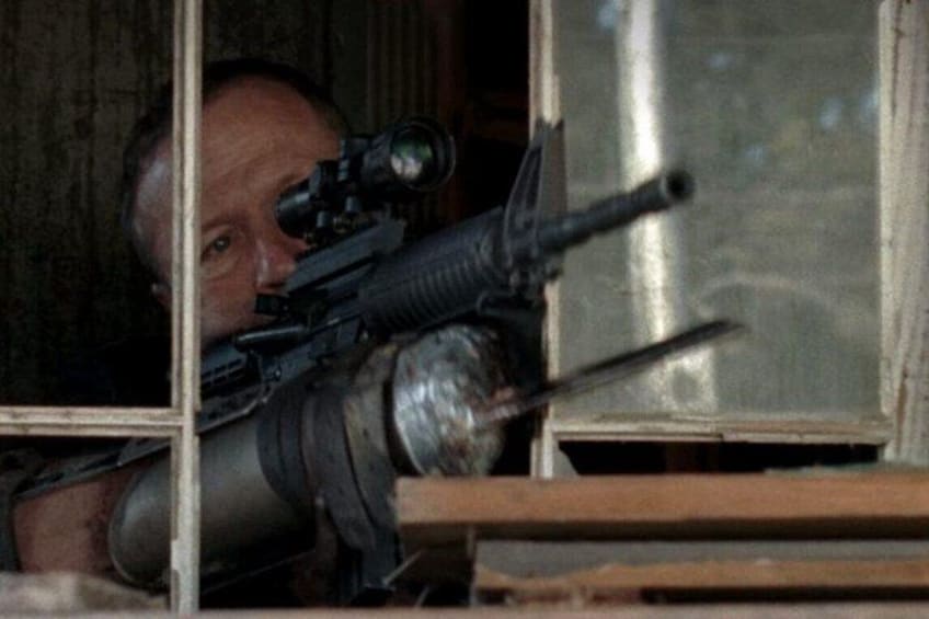 A person aiming a rifle through a window. 2