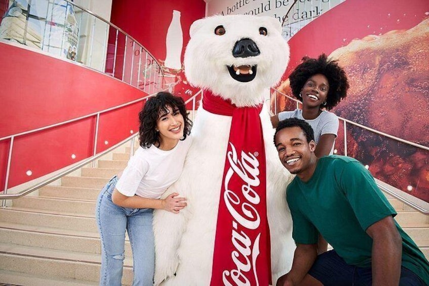 En person utklädd till isbjörn, med en Coca-Cola-logotyp, som står på en trappa med röda räcken. 4