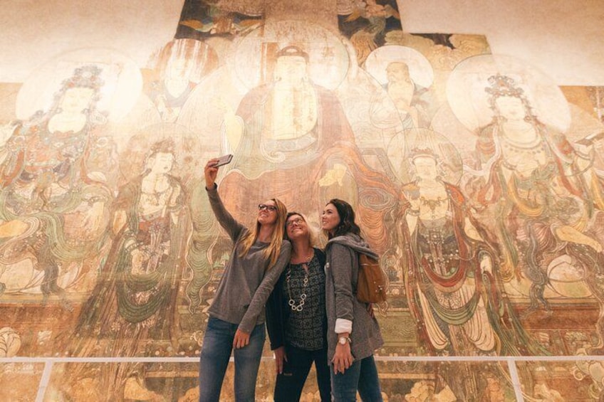 Tres personas tomándose un selfie frente a un mural grande. 2