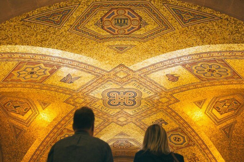Two people observing a detailed mosaic ceiling with geometric patterns and a central emblem. 2