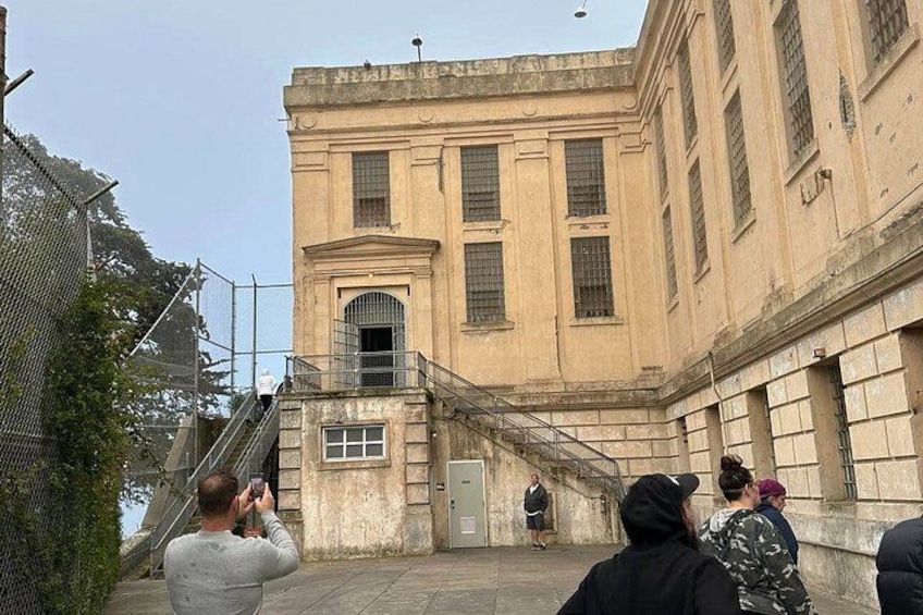 A historic building with a central entrance, a staircase leading up to it, and a fence in the foreground. 4