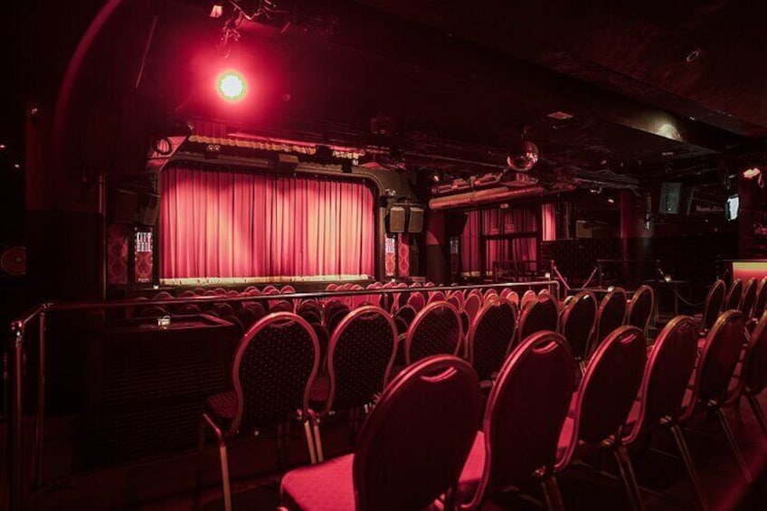 Un teatro con una tenda rossa, file di sedie e un palcoscenico illuminato. 5