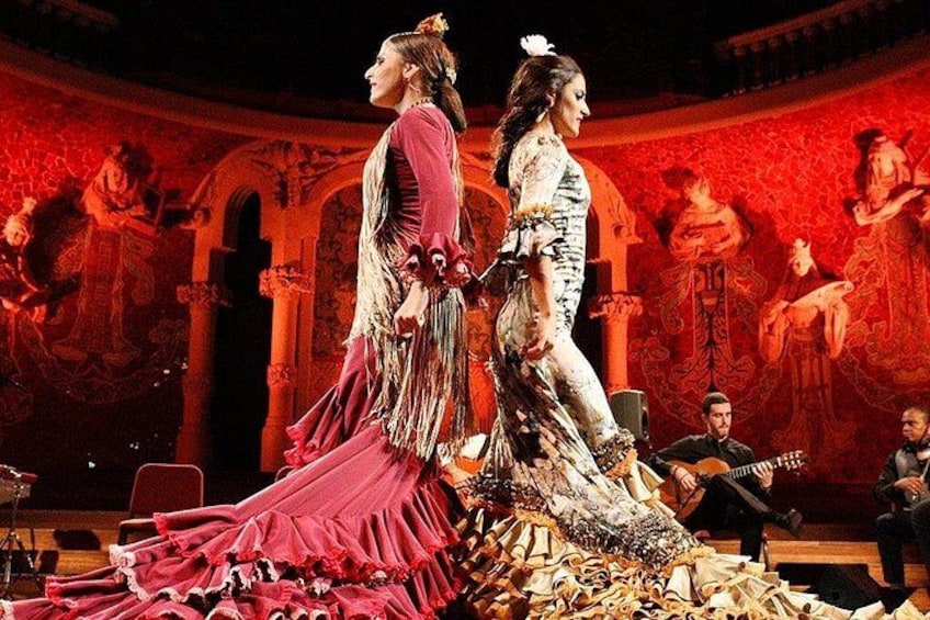 Two women in elaborate costumes on a stage with a classical painting backdrop. 3