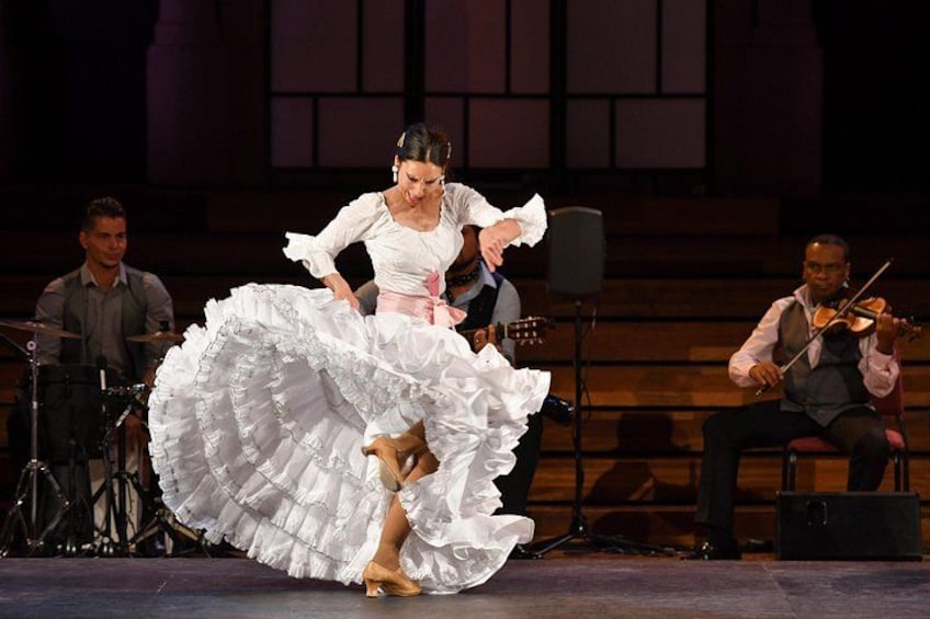 A woman in a white dress dancing on stage with a band. 1