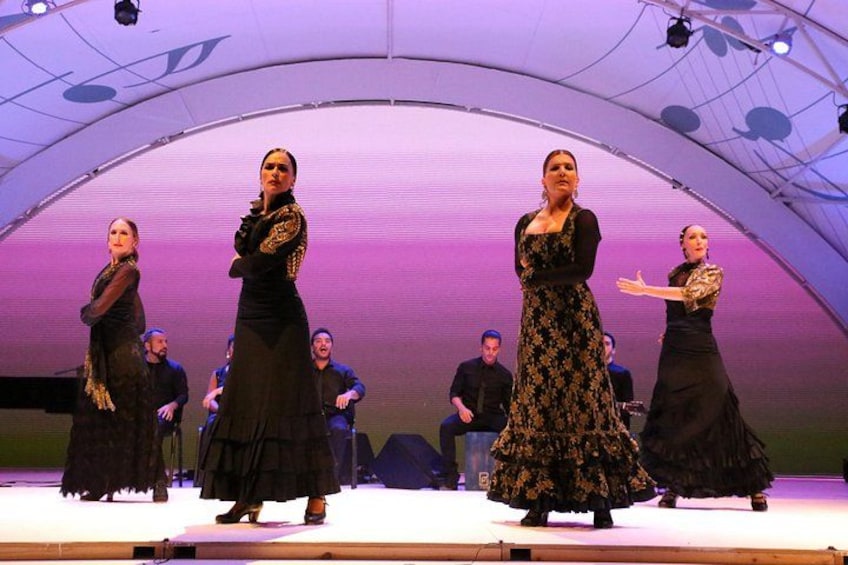 A stage with performers in black dresses, a large arched structure, and a backdrop with a purple hue. 2