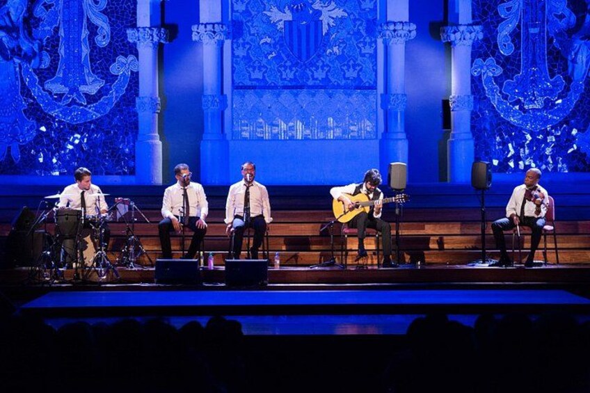 A stage with musicians performing, a large blue decorative backdrop, and a crowd in the foreground. 3
