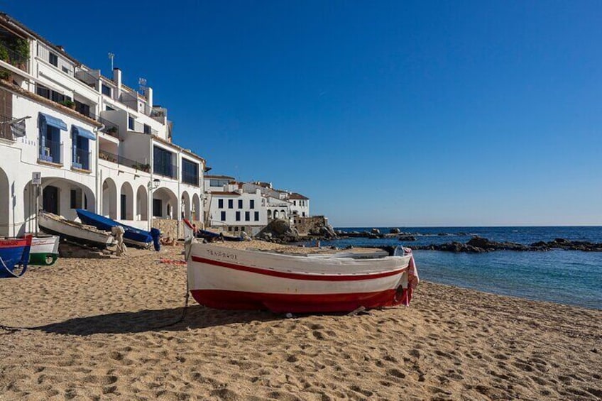 A beach with a red and white boat, white buildings, and a clear blue sky. 1