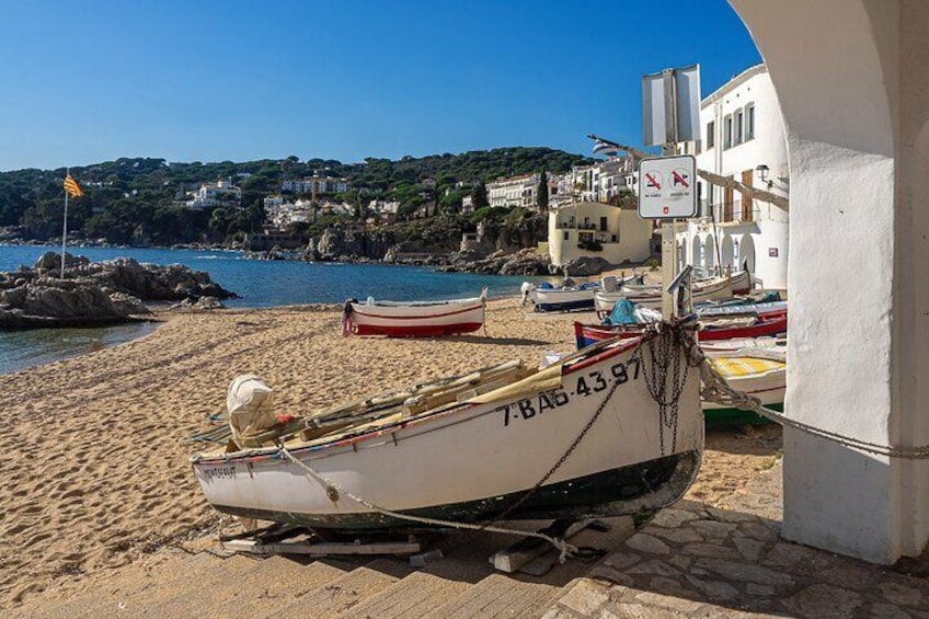 A beach with several small boats tied to a structure, a clear blue sky, and buildings in the background. 4
