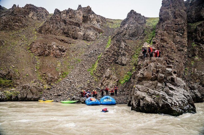 A group of people on a rocky mountain, some on a blue raft, and a river below. 3