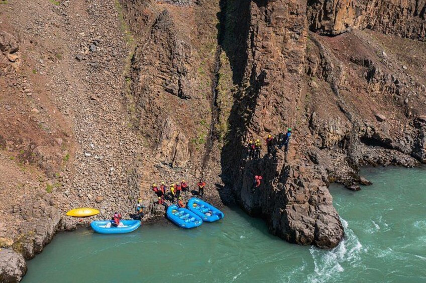 A group of people rafting on a river, with a rocky cliffside and a narrow passage. 2