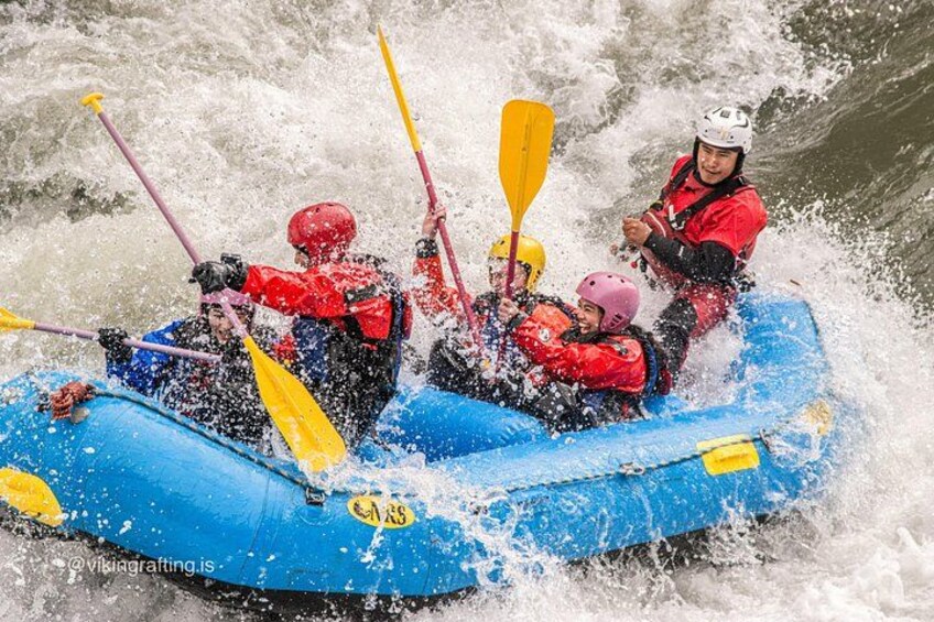 A group of people in a blue raft navigating through rough waters, using paddles. 1