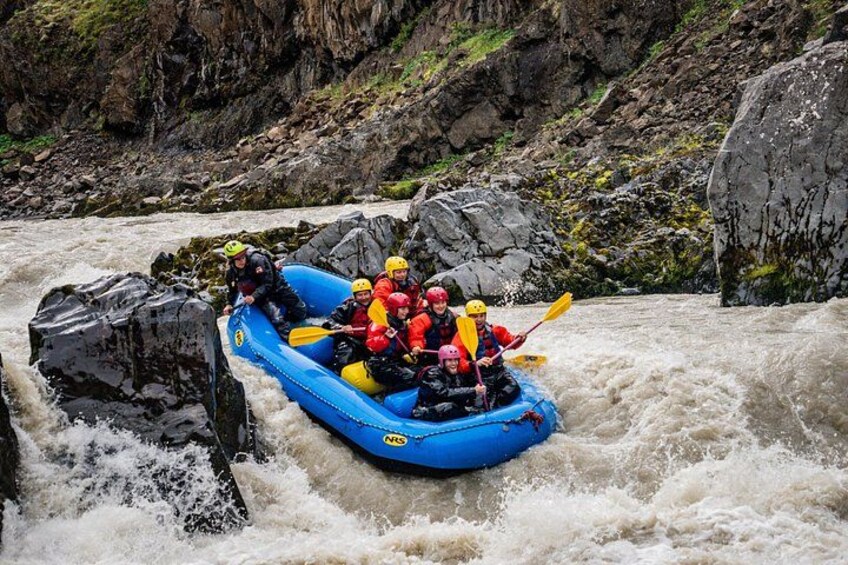 A group of people in a blue inflatable raft navigating a river with rapids. 2