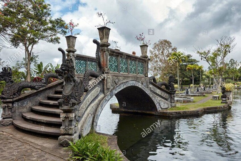 A stone bridge with dragon sculptures, a pond, and a green fence in a park. 3