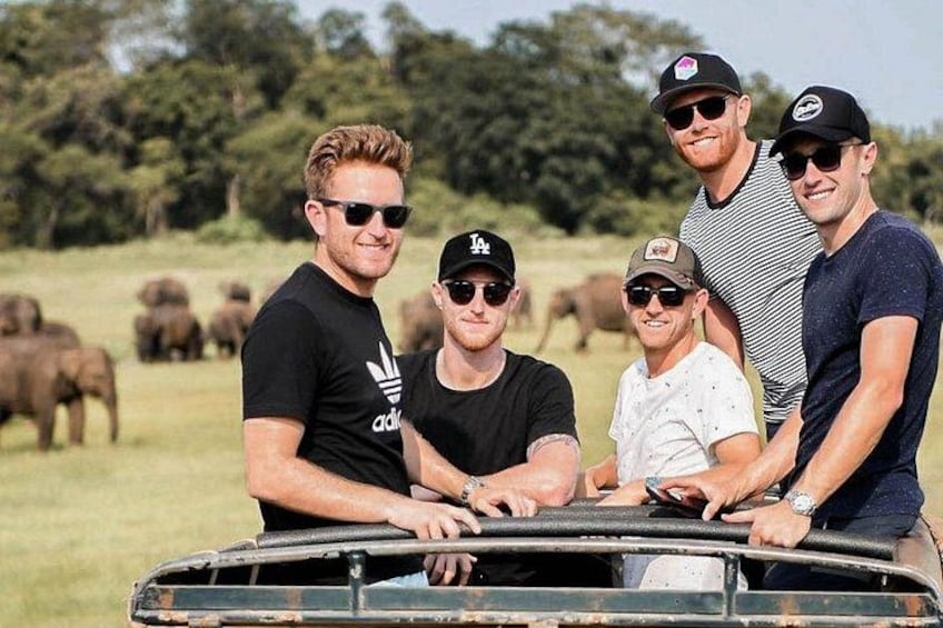 Un grupo de personas en un vehículo safari con elefantes al fondo. 1