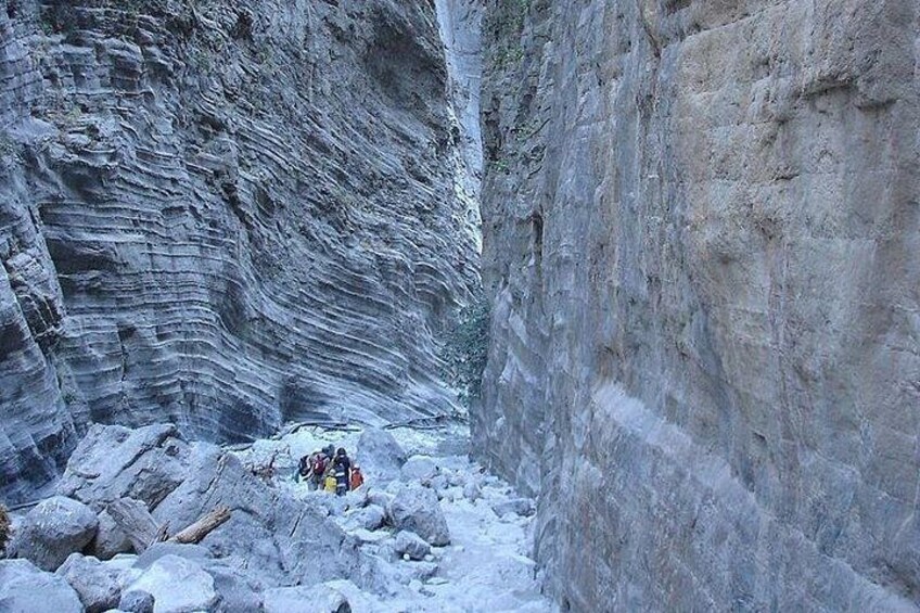 A narrow canyon with layered rock formations and a group of people with backpacks. 1