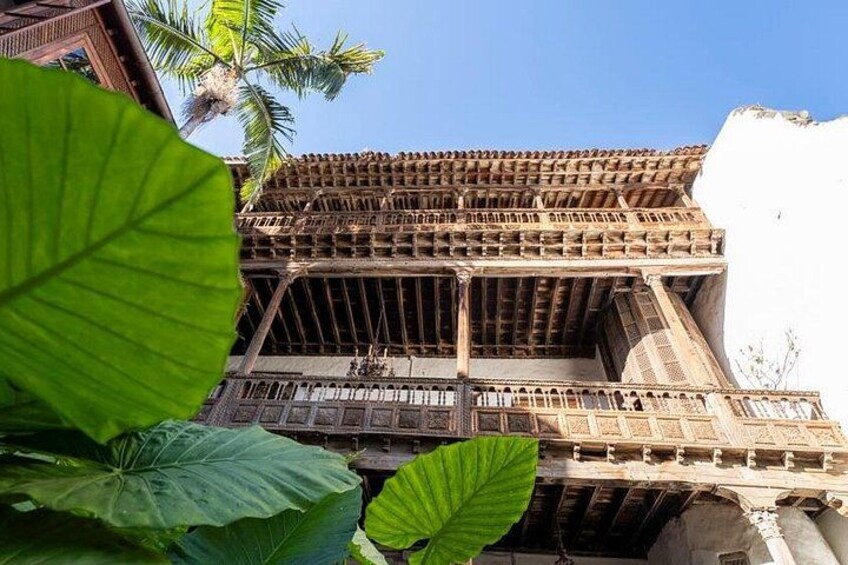 A traditional wooden structure with a sloped roof and multiple balconies, surrounded by lush green foliage. 2