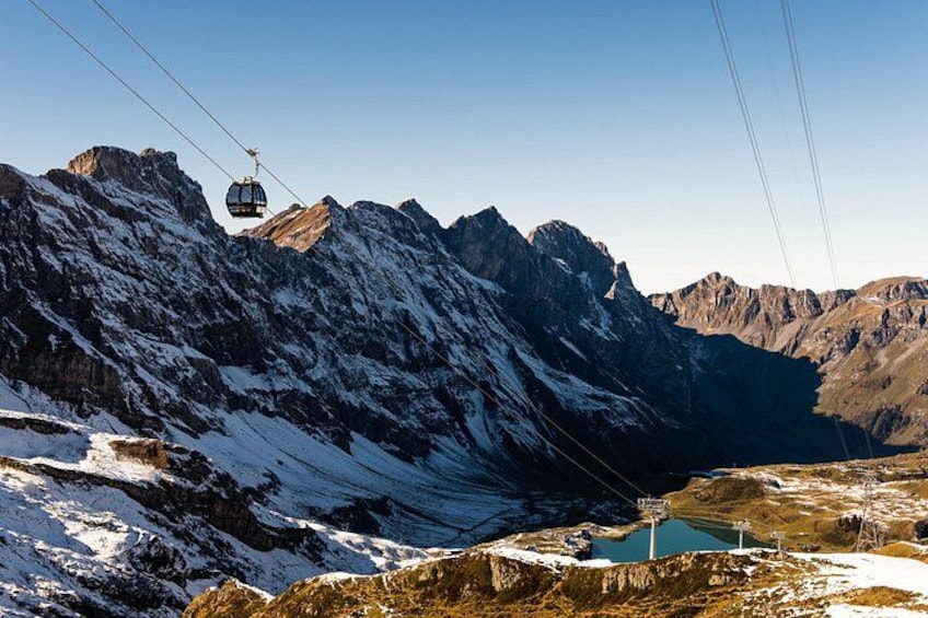 Un teleférico se desplaza sobre un paisaje montañoso con picos nevados y un valle debajo. 2