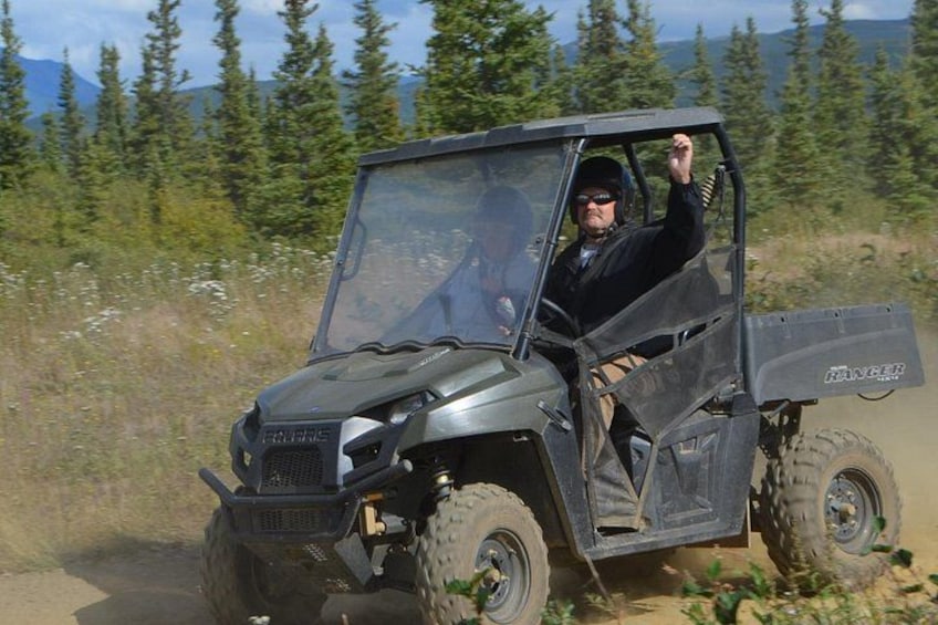 Un vehículo todo terreno Polaris Ranger en un camino de tierra con árboles y montañas al fondo. 1