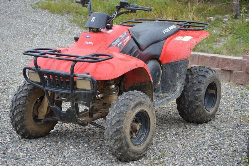 A red ATV with a black seat and side storage, parked on gravel. 2