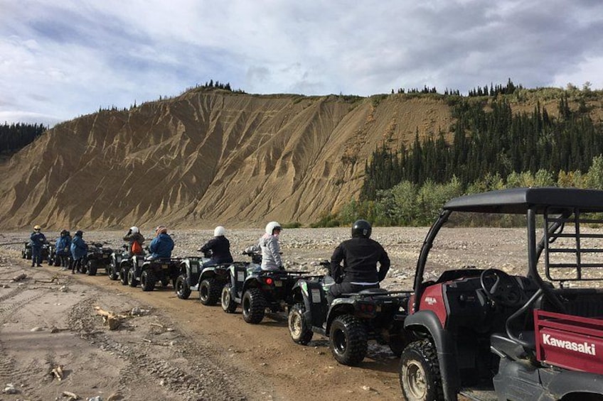 A line of ATVs on a dirt path with a hilly landscape in the background. 3