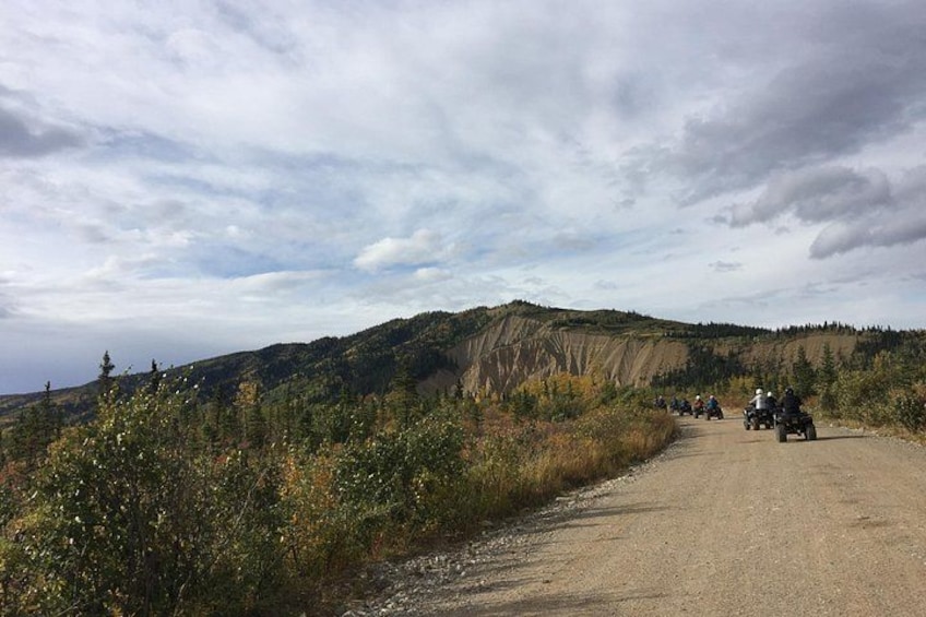 A dirt road with a group of people on motorcycles, surrounded by forested hills. 4