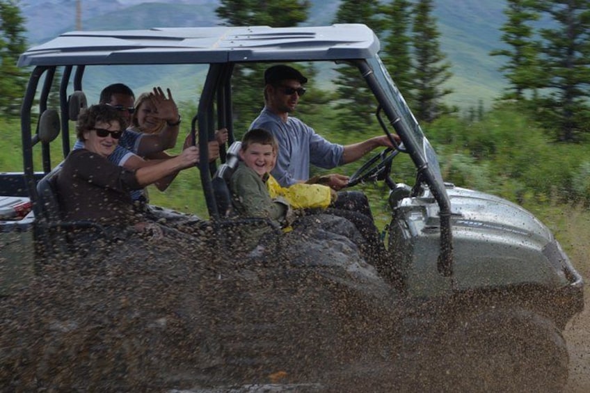 A vehicle with people inside, driving on a road with a mountainous landscape in the background. 1