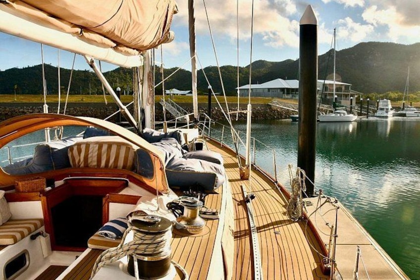 A sailboat docked at a marina with a wooden deck, cushions, and a small table with a pitcher. 2