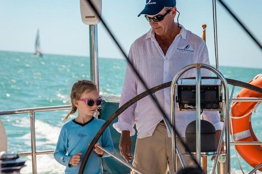 A person steering a boat, another person standing beside them, and a lifebuoy on the deck. 5
