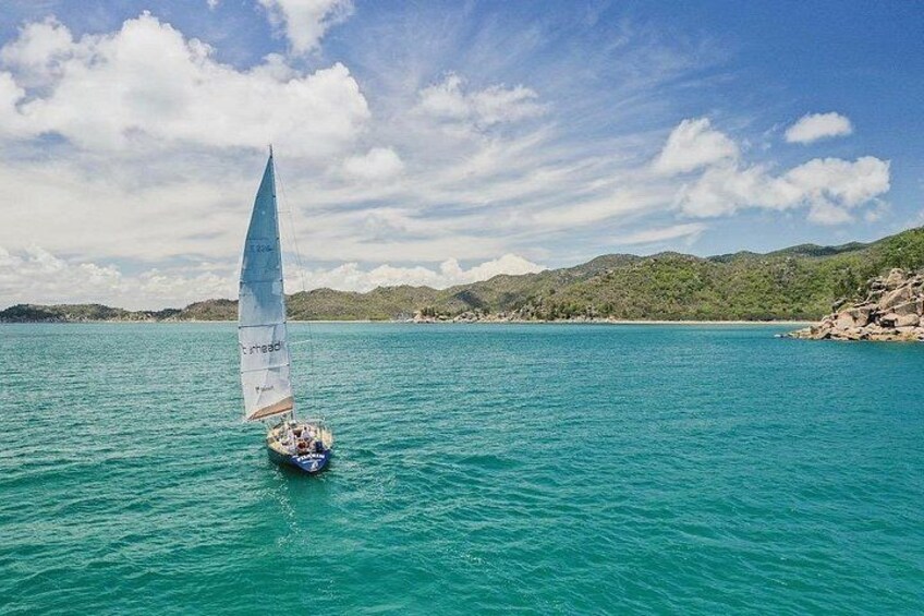 A sailboat on turquoise water with a mountainous coastline in the background. 3