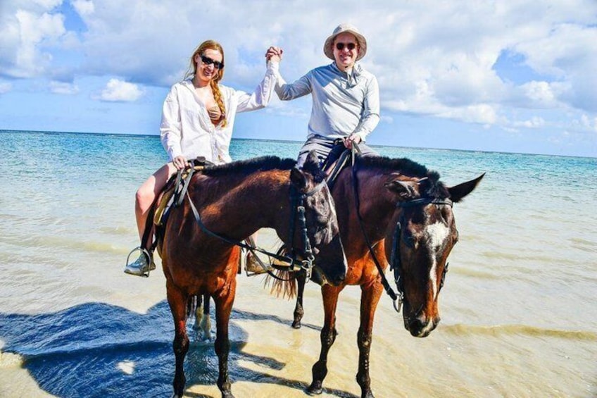 Two people riding horses on a beach with clear water and a cloudy sky. 4